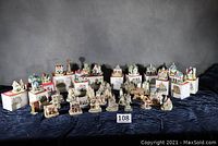 Group of over 35 miniature collectible houses, some boxed, some loose, arranged on a dark surface against a dark backdrop.