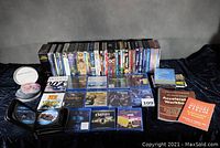 Photo showing a broad lot of DVDs and Blu-ray discs arranged on black cloth including various titles and sets, some sealed.