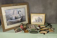 Wide shot of entire lot including framed prints, wooden ducks, decorative tile, and book displayed on green surface.
