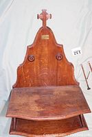 Full view of the oak wall-mounted Bible stand showing the shaped back panel with cross, foldable angled shelf, and lower shelf