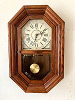 Full view of the wooden framed chime wall clock showing entire clock including pendulum and glass door.