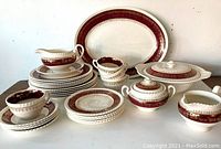 Vintage Sovereign Potters earthenware dishes arranged, showing variety of plates, cups, serving dishes with red and gold decorative pattern.