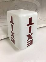 White glass light shade with red 'EXIT' lettering on three sides, showing the shape and lettering clearly.