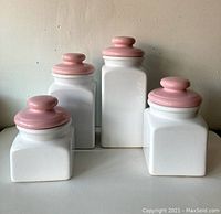 Four vintage ceramic canisters with white square bodies and pink lids in varying sizes, showing overall set.