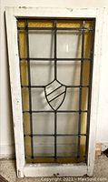 Full front view of the antique leaded glass window with amber stained glass border and central shield design.