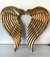 Front view of the gold-colored metal wing wall decor showing feather details and overall shape.