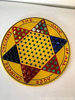Full round metal Chinese checkers board showing six colored triangular sections with marbles and printed text around.