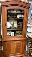 Front view of the tall antique cabinet showing the original wavy glass door revealing shelves with decorative items inside and a solid wood lower door with carved design.