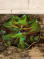 Top view of the ruffled art glass plate showing the colorful swirl pattern with green, brown, and blue hues.