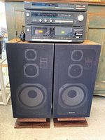Front view of the Technics stereo system stacked components and two large floor-standing speakers on wooden platforms.