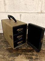 Front view of closed vintage slide case showing fabric cover and black handle on top.