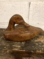 Side view showing the full body and head of the wooden duck decoy on a rustic surface.