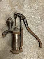 Overview photo showing the full vintage metal pump with curved lever and bulbous spout, laying on concrete floor.