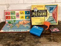 Group photo showing all games including Pirate and Traveler Game board, Puz-Game box, Hi-Q case, Paddle Peal orange cup, and poker chips on wooden surface against white brick wall.