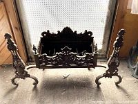 Front view of the large cast iron fireplace insert showing ornate scrollwork and leaf motifs on the grate and side supports with curved legs.