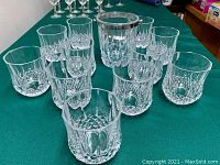 Eleven clear crystal tumblers with detailed cut patterns, arranged on green surface. Two are chipped.