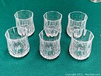 Six clear crystal shot glasses arranged on green cloth, showing diamond-cut base and smooth upper section