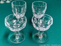 Two Waterford crystal water glasses and two dessert bowls on green cloth background.