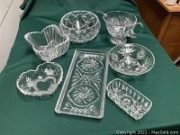 Photo showing all assorted crystal and cut glass bowls and dishes laid out on green fabric, displaying a variety of shapes including heart, round, rectangular, and scalloped edges.