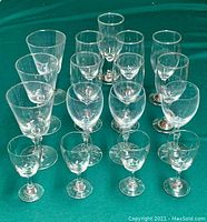 Overview of 17 clear glass stemware arranged on a green surface showing different sizes and shapes, including rounded and straight-sided bowls.