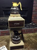 Front view of the Silex Koffee-King coffee maker showing the upper glass pot with yellow handle and lower glass pot with black handle on the unit.