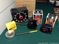 Overall view of the vintage darkroom timer, safelight, film loader, film tin, and thermometer arranged on a green table, several items in original packaging visible.