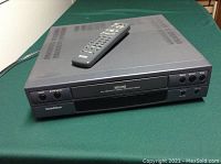 Front view of Goldstar VHS player with remote control on top showing buttons and VHS slot.
