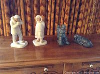 Four Native Canadian and Alaskan figurines lined up on a wooden surface against a bamboo-style wall background.