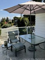 Patio set on balcony showing glass-top table, umbrella, lounge chair and footstool
