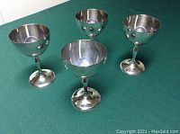 Four silverplate wine glasses shown from above and side, placed on green surface.