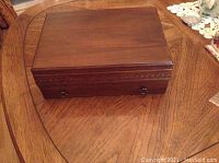 Closed polished wood case with smooth finish and brass hardware, placed on wooden table.