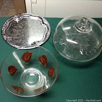 Photo of three vintage serving pieces: metal tray, glass chip bowl with brown leaf accents, and glass cake plate with clear cover and etched floral design.