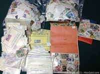 Photo showing two large plastic bags filled with loose stamps, multiple stamp albums, individual sheets and packets containing various vintage stamps from multiple countries.