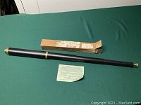 Photo of the vintage telescope with brass ends, original box, and instruction paper on a green surface.