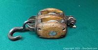 Large vintage wooden block pulley with three sheaves and metal hook resting on a green cloth background