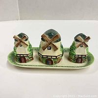 Front view of the three windmill ceramic shakers and matching base tray on a white background.