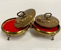 Top view showing two open round compartments with red velvet interiors and hinged decorative brass lids with leaf/feather motifs.