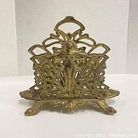 Front view of the brass Art Deco letter or napkin holder showing the central female figure and intricate filigree design.