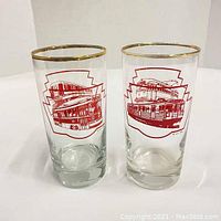 Front view of 2 glasses with red TTC transit images and gold rims on white background.