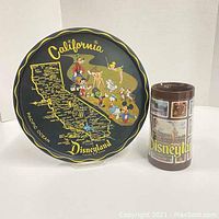 Front view of round metal tray with California map and Disney characters next to tall Disneyland Thermo-Serv mug.