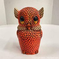 Front view of the vintage ceramic owl piggy bank showing textured orange and brown scale pattern and prominent black and yellow eyes.