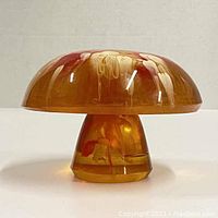 Front view of the mushroom paperweight showing amber acrylic with internal swirls in cream and red hues.