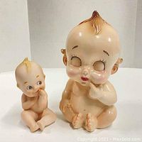 Front view of both Kewpie ceramic items showing the larger vase and smaller figurine with similar skin tone and painted details.