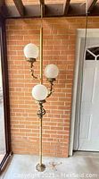 Full view of the brass tension pole lamp showing three globe lights and base