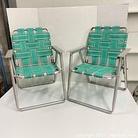 Front view of two vintage children's lawn chairs with aluminum frames and green woven webbing seats and backs.