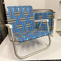 Front and side view of two vintage folding aluminum beach chairs showing blue multicolor webbing and silver frames with white armrests.
