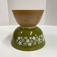 Two vintage Pyrex mixing bowls stacked, smaller brown bowl on top of larger green bowl, showing overall colors and patterns