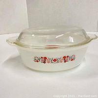 Side view of Fire King Primrose casserole dish with clear glass lid on top showing floral pattern and white milk glass body.
