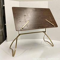 Front view of the vintage adjustable cookbook or artwork stand showing wooden panel with adjustable metal arms and brass-colored metal base.