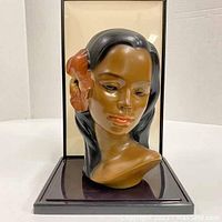 Front view of the vintage mid-century modern Hawaiian head bust mounted on a dark plastic base with backing.
